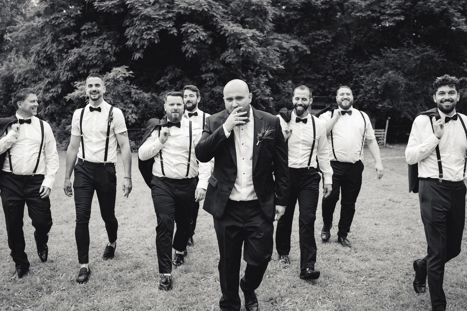Photo de groupe mariage le marié avance en fumant une cigarette suivi des ses témoins tous alignés en costume chemise bretelles noeud pap