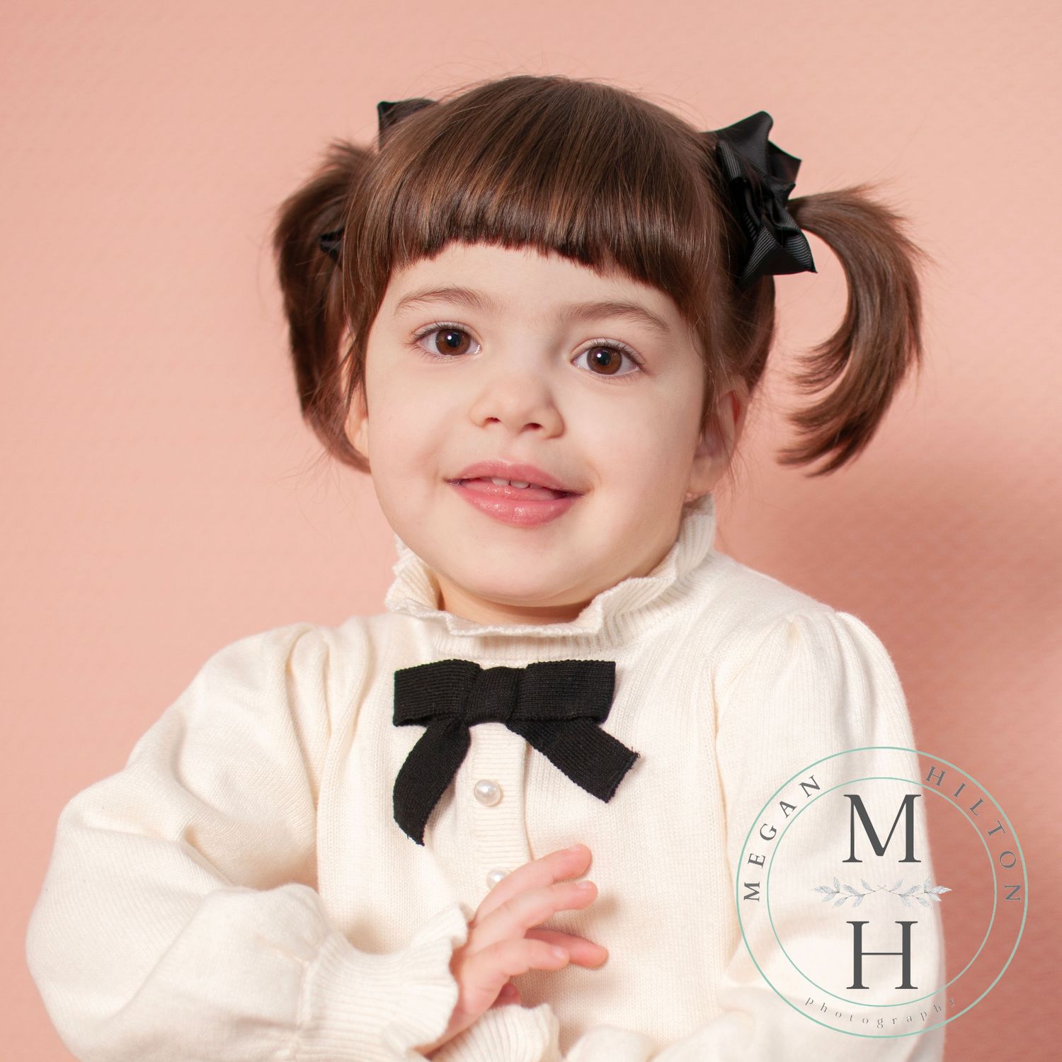Smiling photo of a three year old girl wearing ivory on a peach background