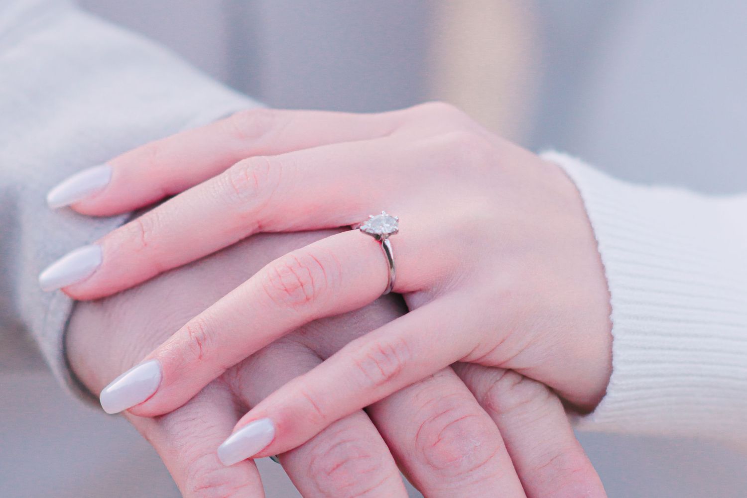 Close-up of hands showing engagement ring with white sweater sleeves.