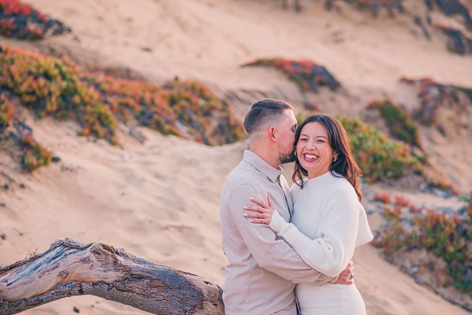 Couple laughing together during sunset engagement photo session on sandy hill.