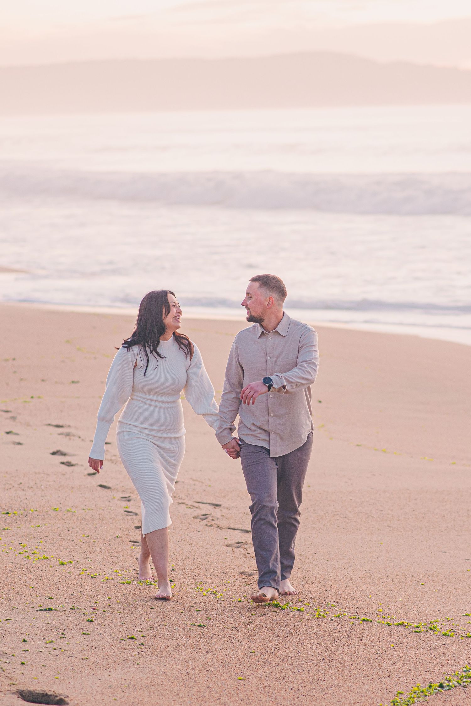 A couple takes a romantic stroll along a misty beach at sunset.