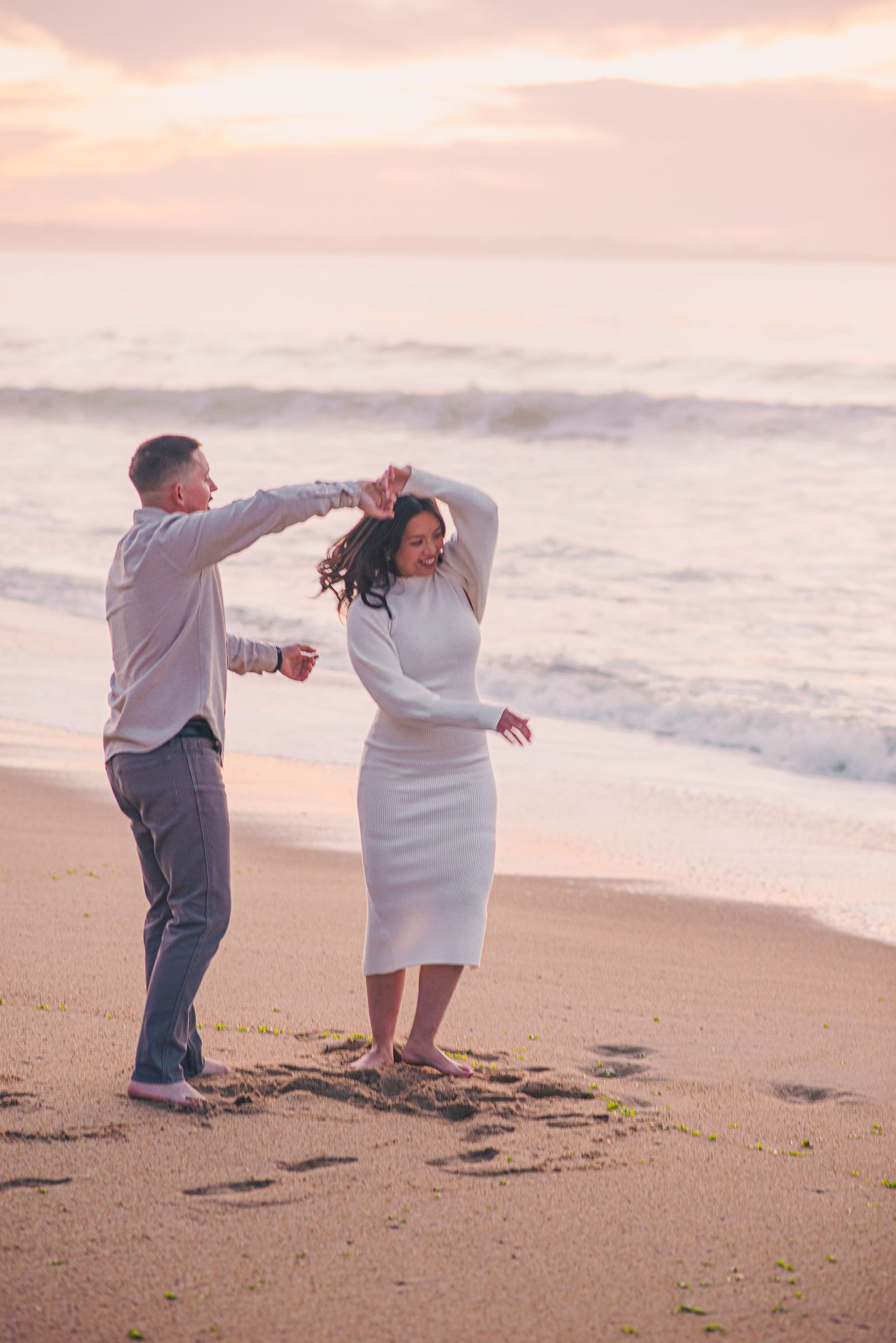 Happy couple dancing together on sandy beach during golden hour.