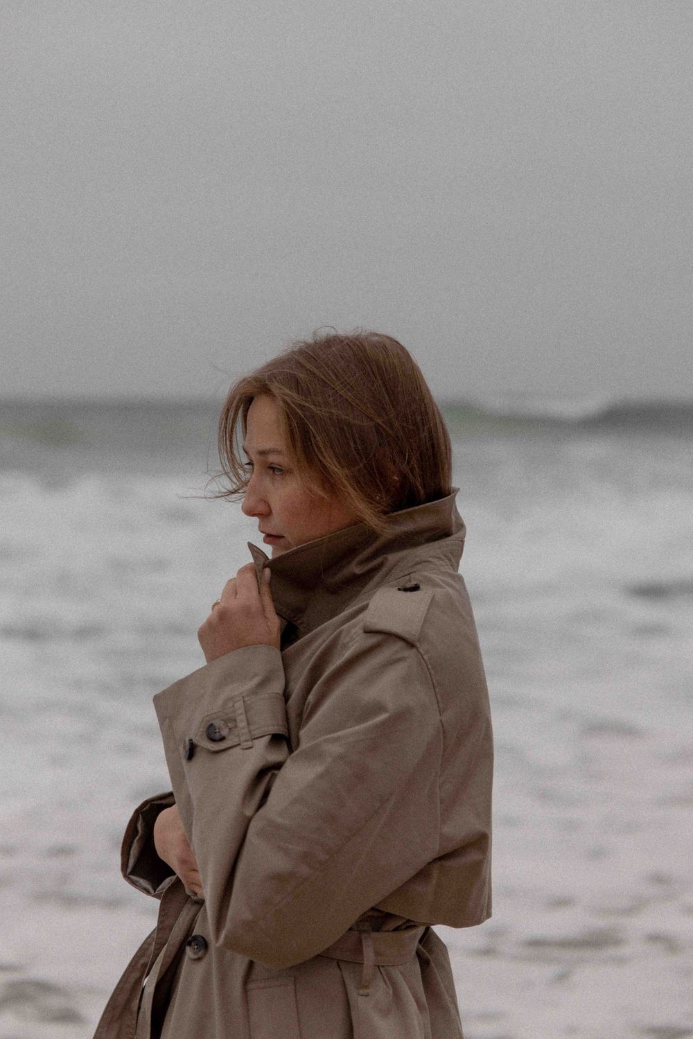 Atmospheric portrait against stormy ocean backdrop in muted tones.