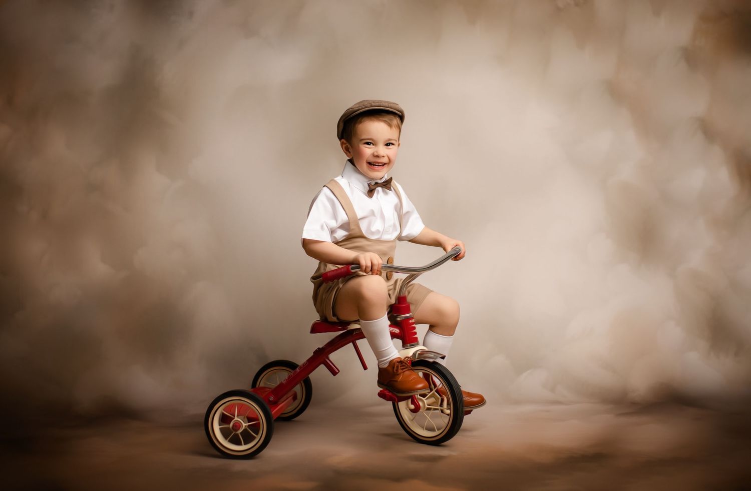 Portrait of a child in vintage style clothing riding a red tricycle against a brown studio backdrop.