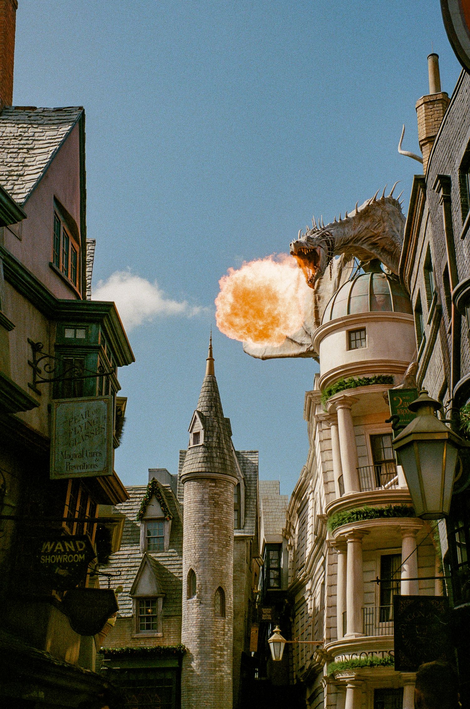 Dragon statue breathing fire against blue sky in a whimsical urban setting.