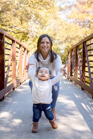 Parent and toddler walking together on wooden bridge during autumn day.