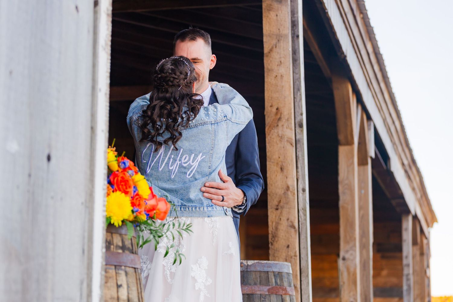Wedding couple embracing in rustic wooden doorway with colorful autumn flower bouquet.