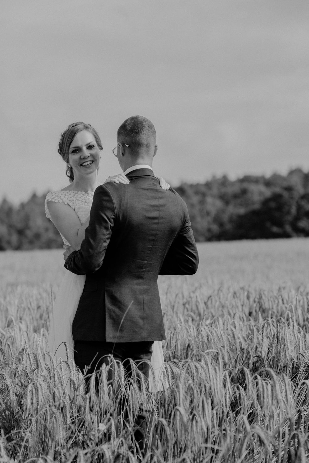 Black and white wedding photo showing a couple standing together in a wheat field.