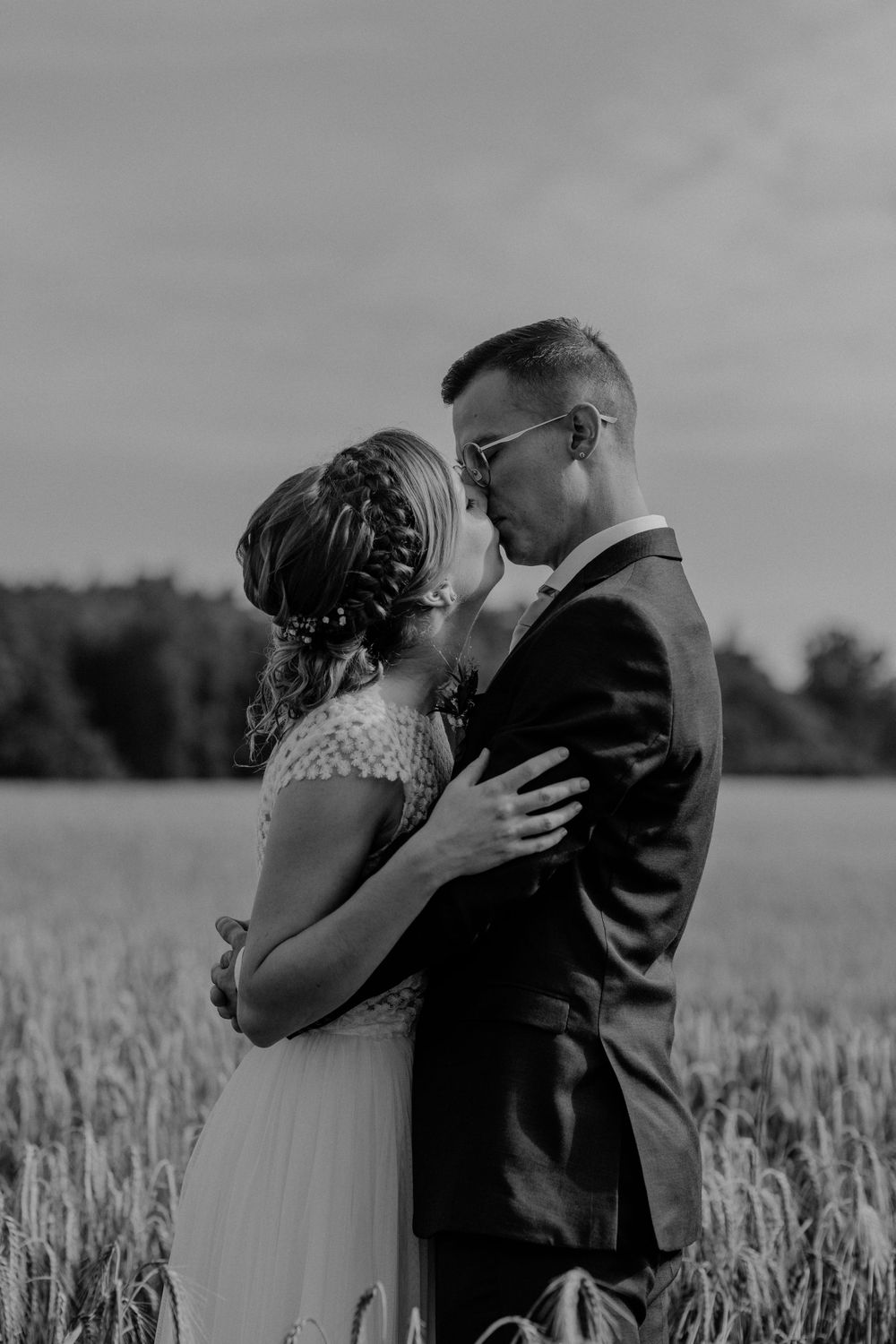 A romantic black and white wedding photo of a couple sharing a kiss in a rural wheat field.