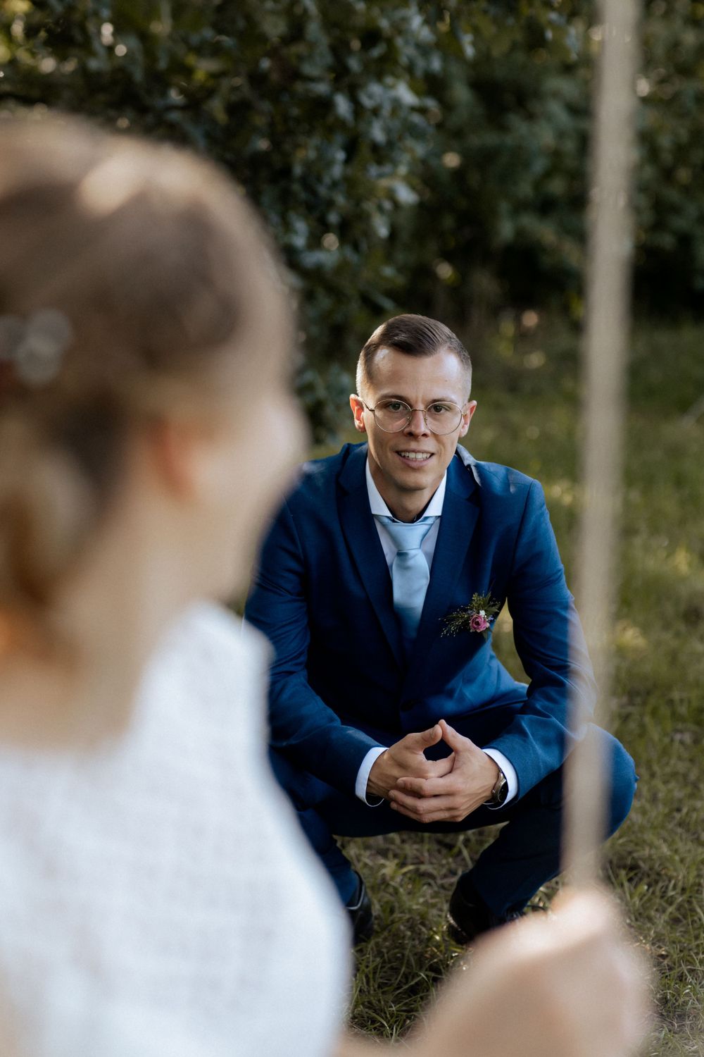 A groom in a navy blue suit smiles while sitting outdoors during a wedding photo session.