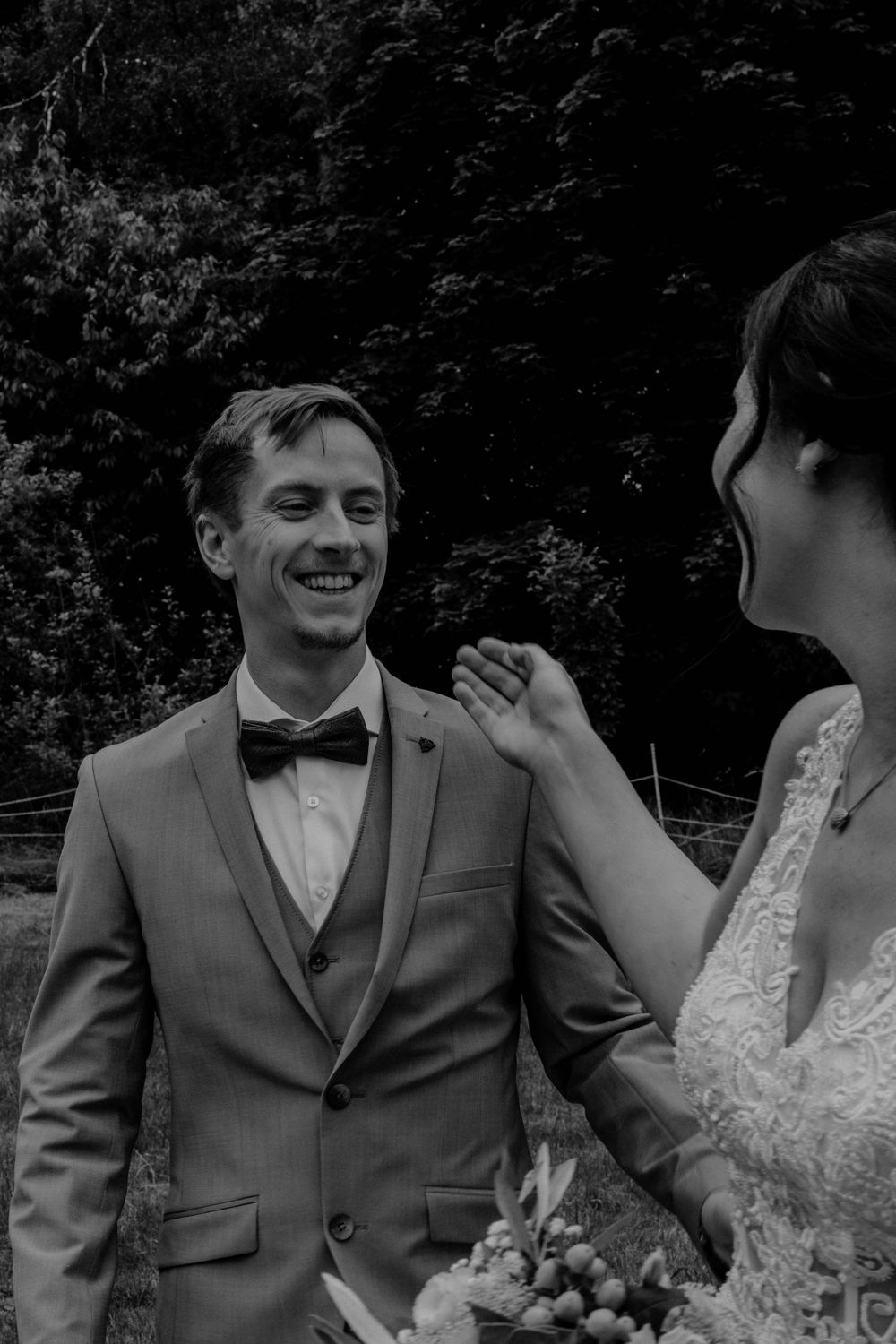 A joyful black and white wedding moment captured between a couple sharing a laugh outdoors in formal attire.