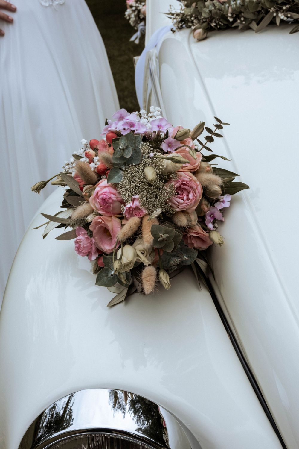Romantic wedding bouquet with pink roses and eucalyptus resting on white fabric against dark background.