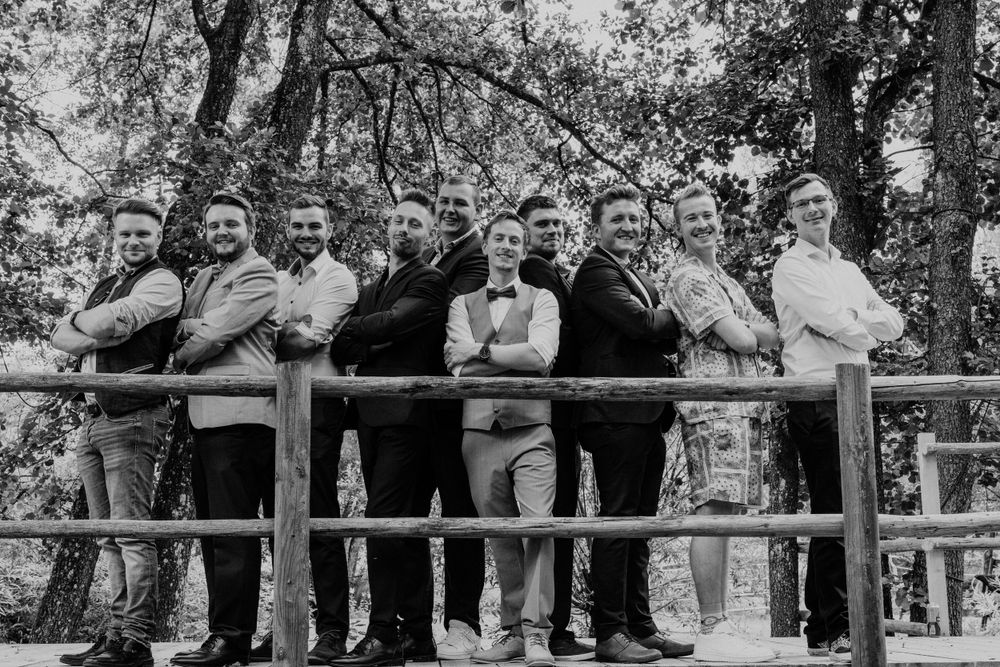 A black and white vintage photograph shows a group of men standing together along a wooden railing outdoors.