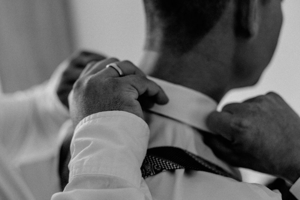 Close-up black and white image of hands adjusting a necktie and white dress shirt collar.