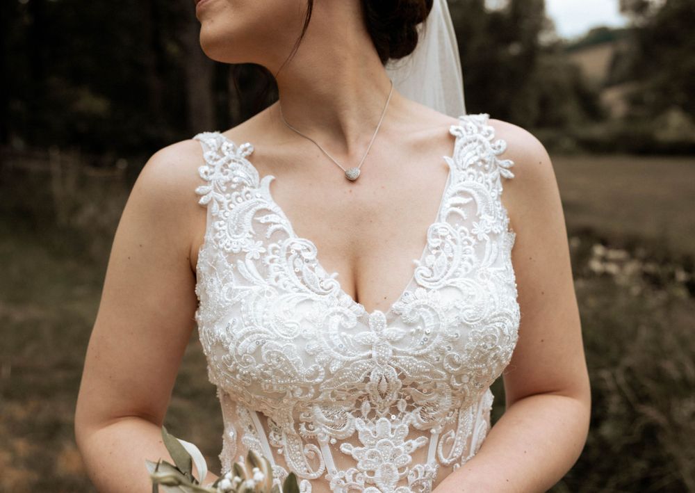 A wedding dress with intricate white lace detailing and delicate V-neckline shown in sepia-toned photograph.