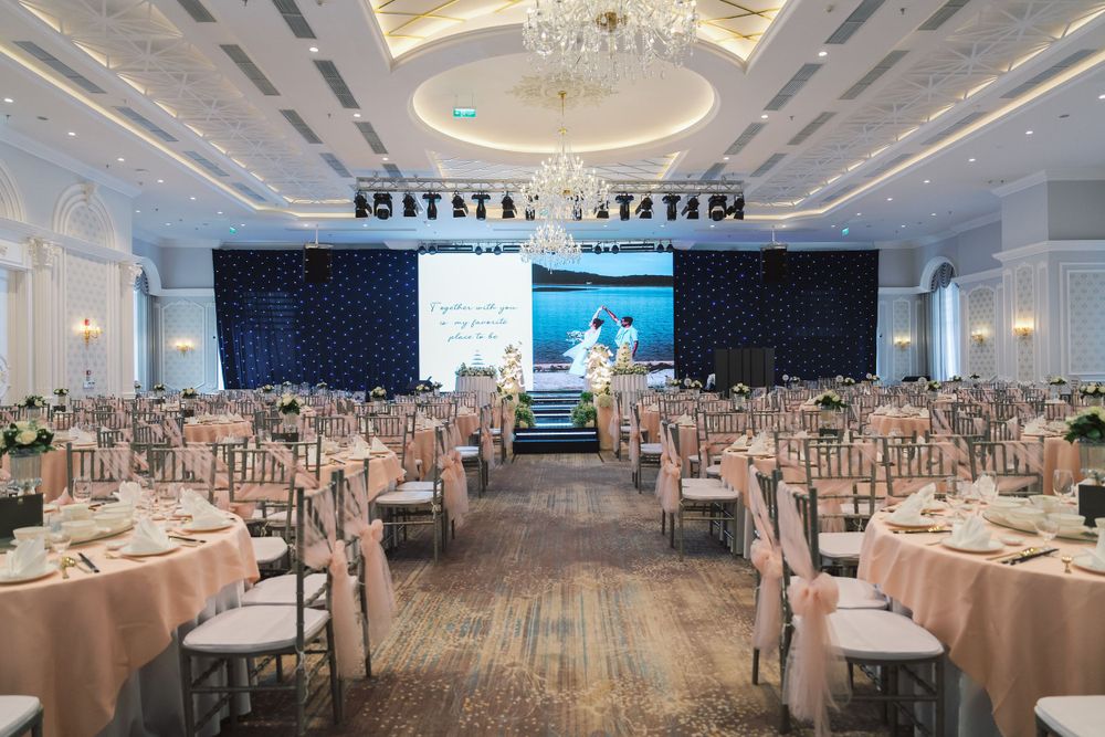 Elegant wedding reception ballroom setup with round tables and stage backdrop.