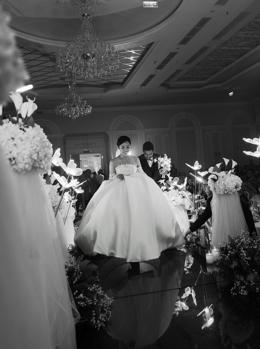 Elegant ballroom wedding scene with bride in flowing gown under crystal chandeliers.