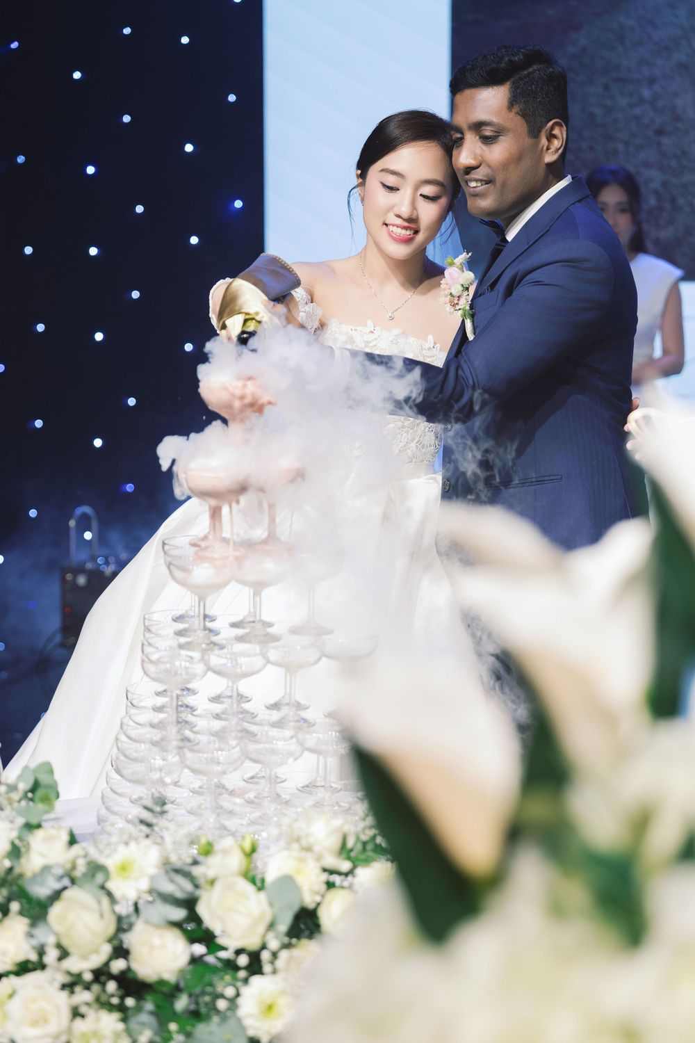 Newlyweds pouring champagne into tower of glasses at reception.