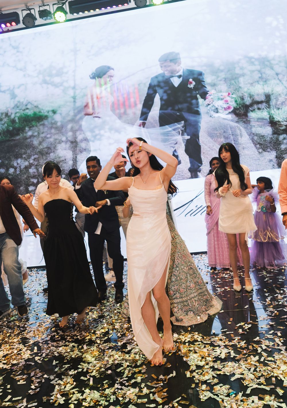 Wedding reception celebration with confetti and projected backdrop showing festive dancing scene.