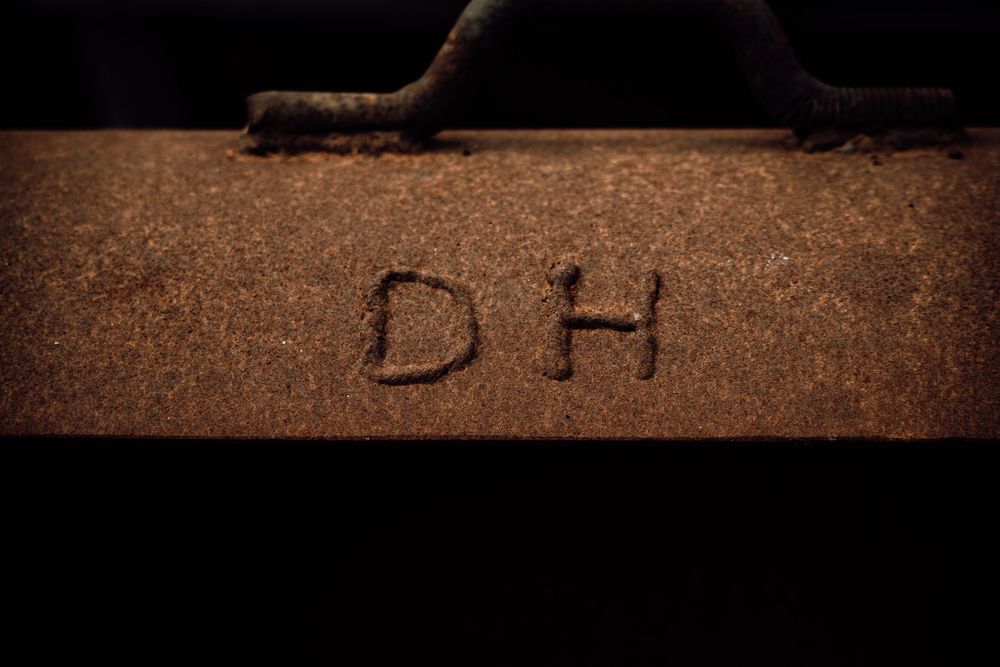 The initials DH carved or written into a rustic wooden surface in warm amber tones.