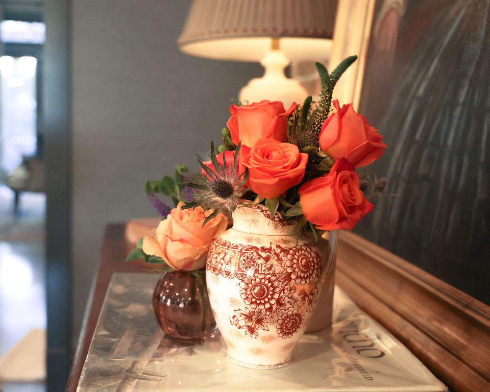 Coral roses displayed in decorative vases with intricate patterns under warm lighting.