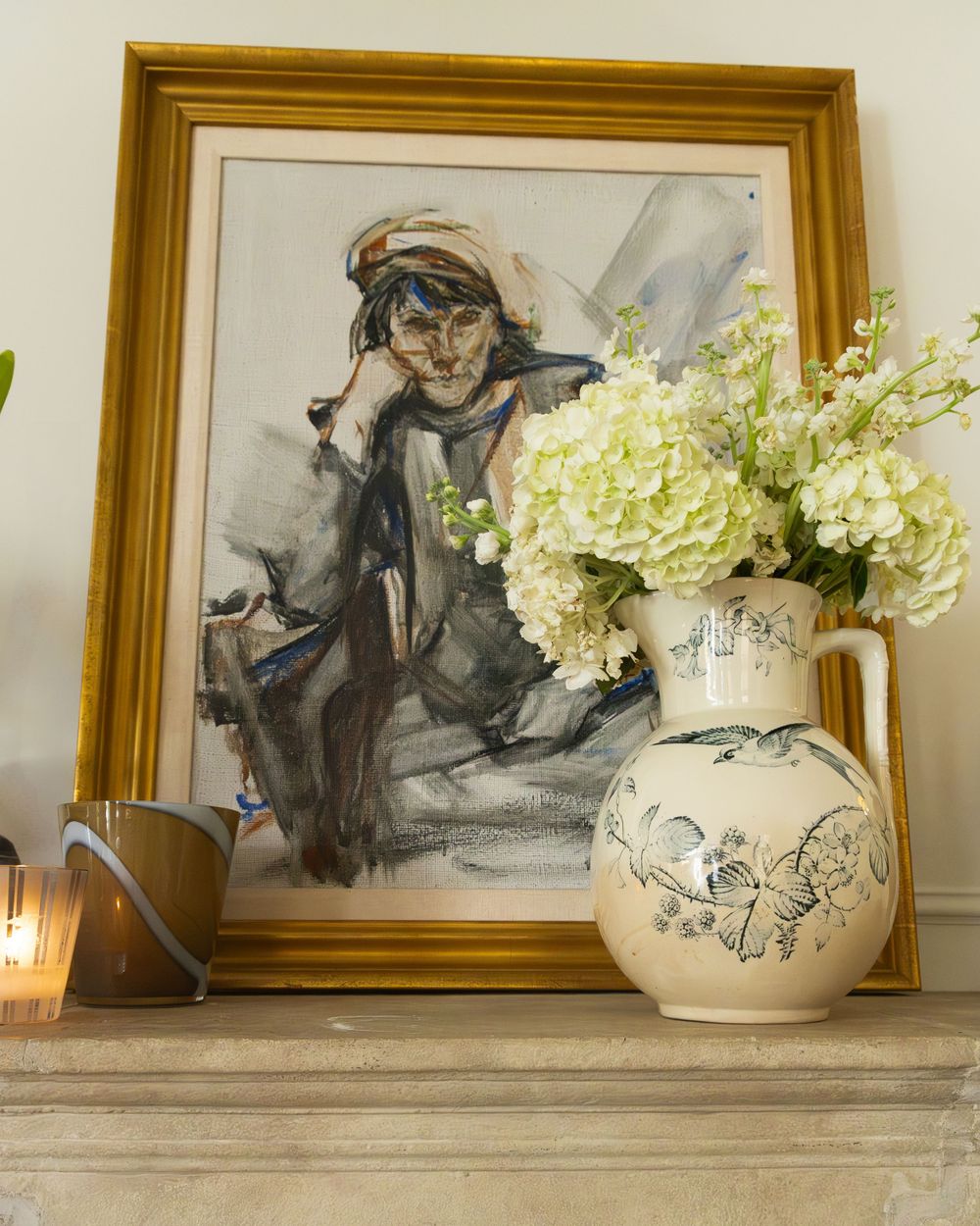 White ceramic vases with sketched artwork displayed in front of framed artwork on a shelf.