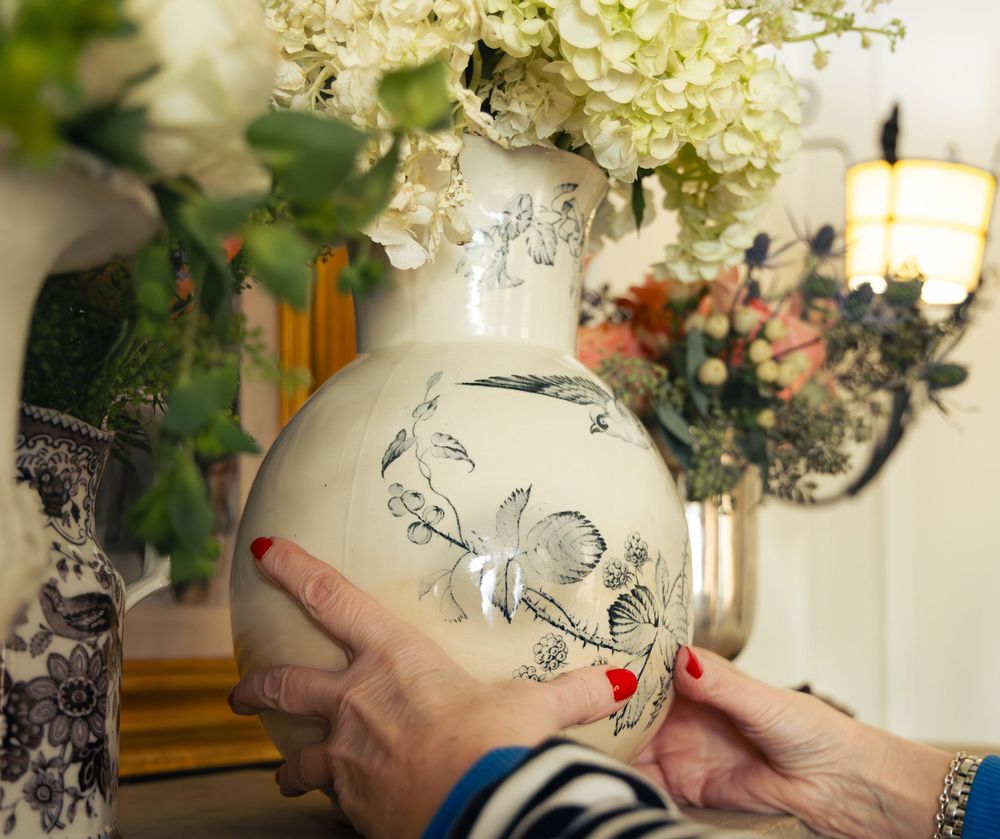 White ceramic vase with decorative illustrations displayed alongside fresh floral arrangements.