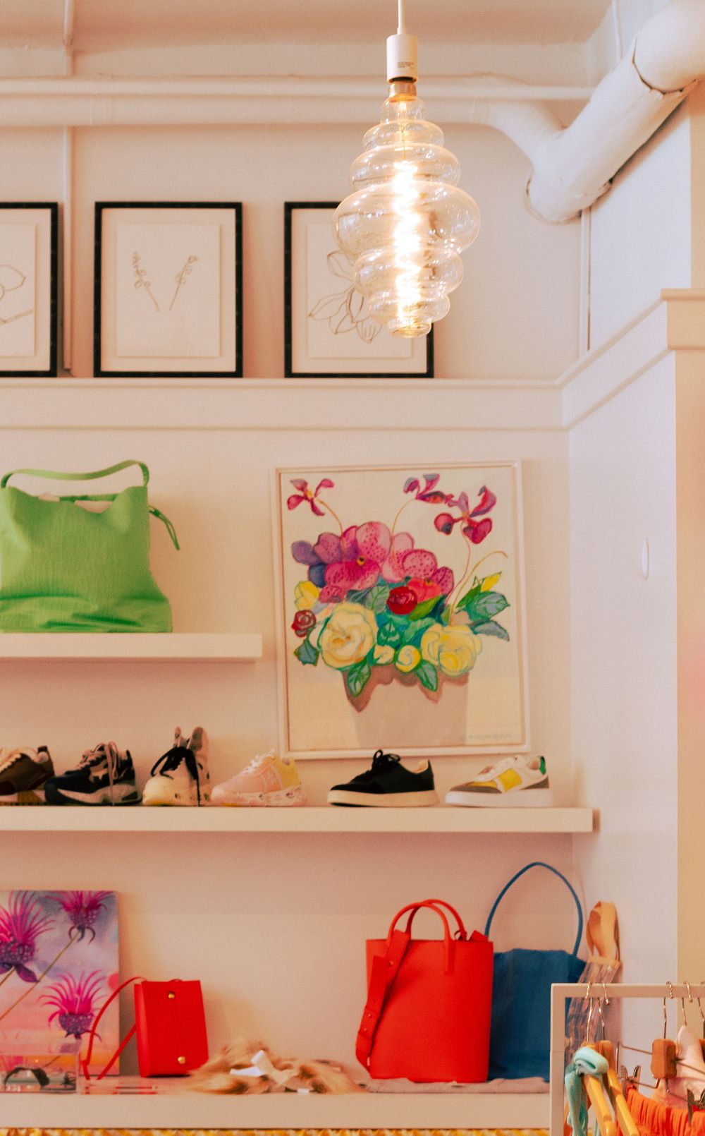 Stylish retail display with hanging glass pendant light, floral artwork, and colorful handbags.