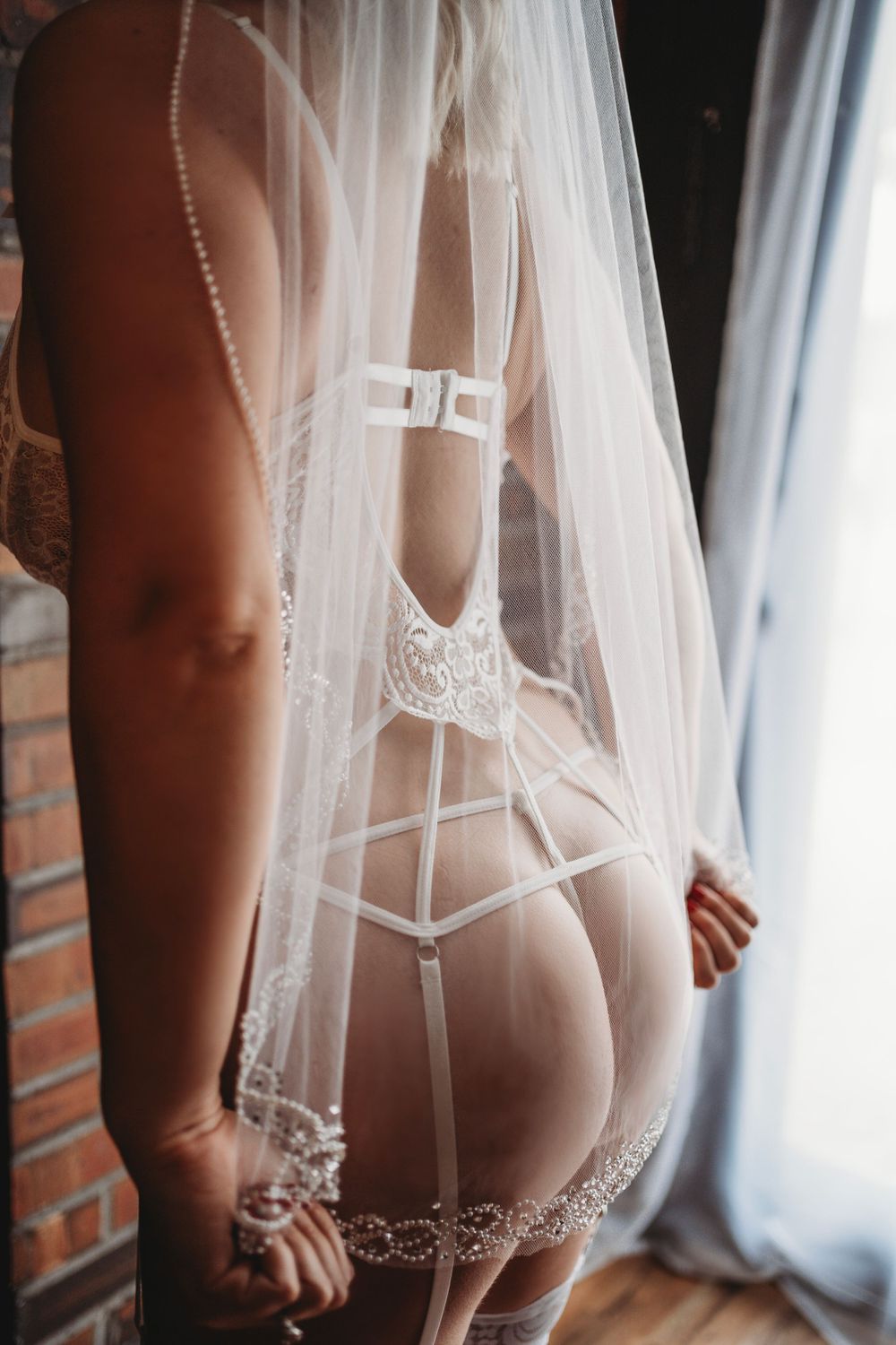 Woman in lace lingerie and veil, holding the fabric, with a seductive pose highlighting her curves and silhouette.