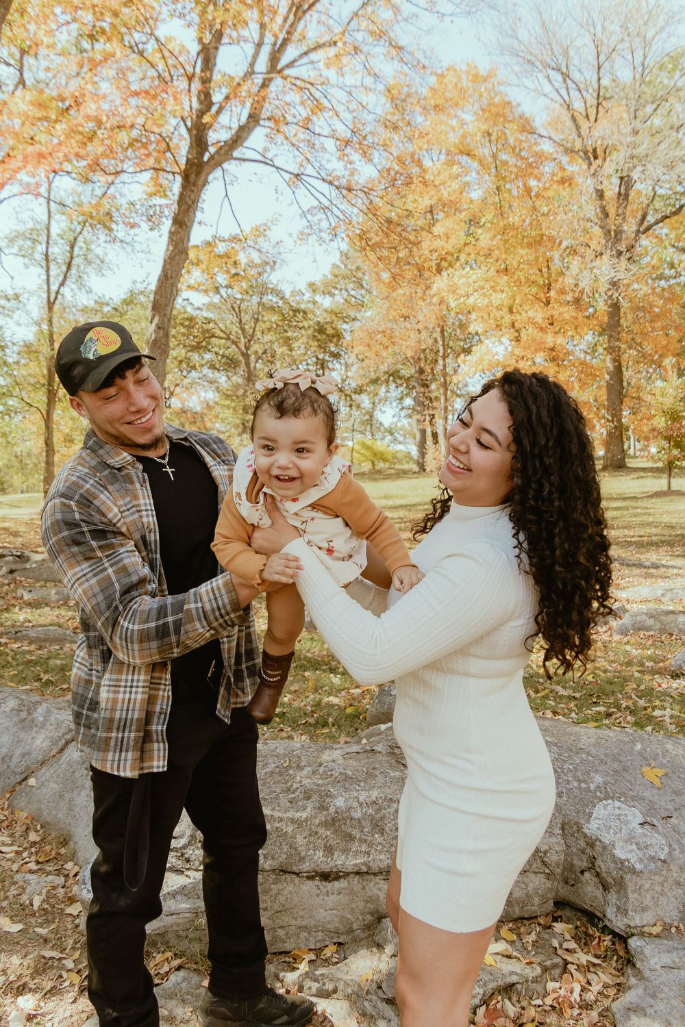 Candid family moment captured in a park with golden autumn leaves in background.