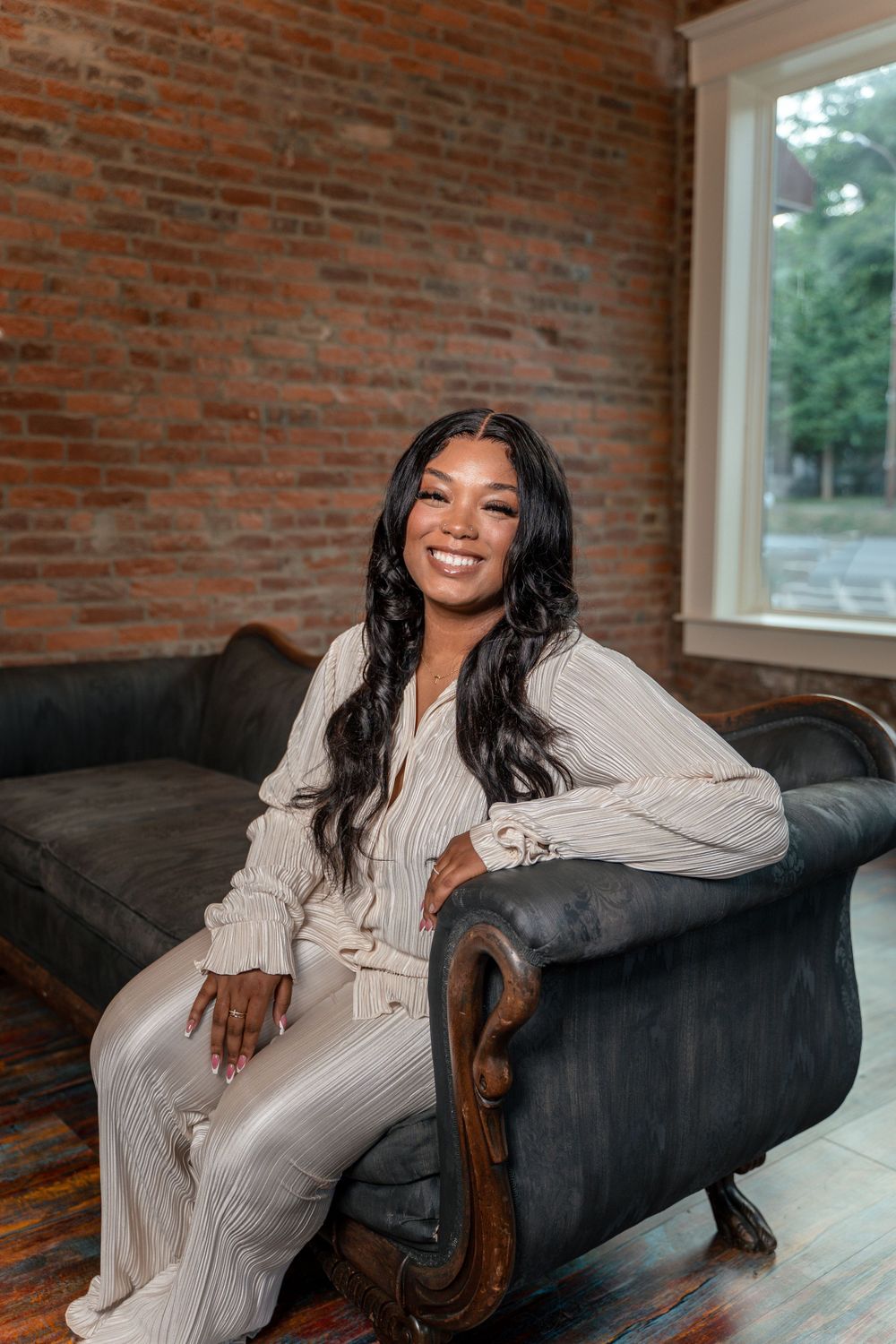 Person in white knit loungewear sitting on vintage leather couch in rustic room with brick walls.