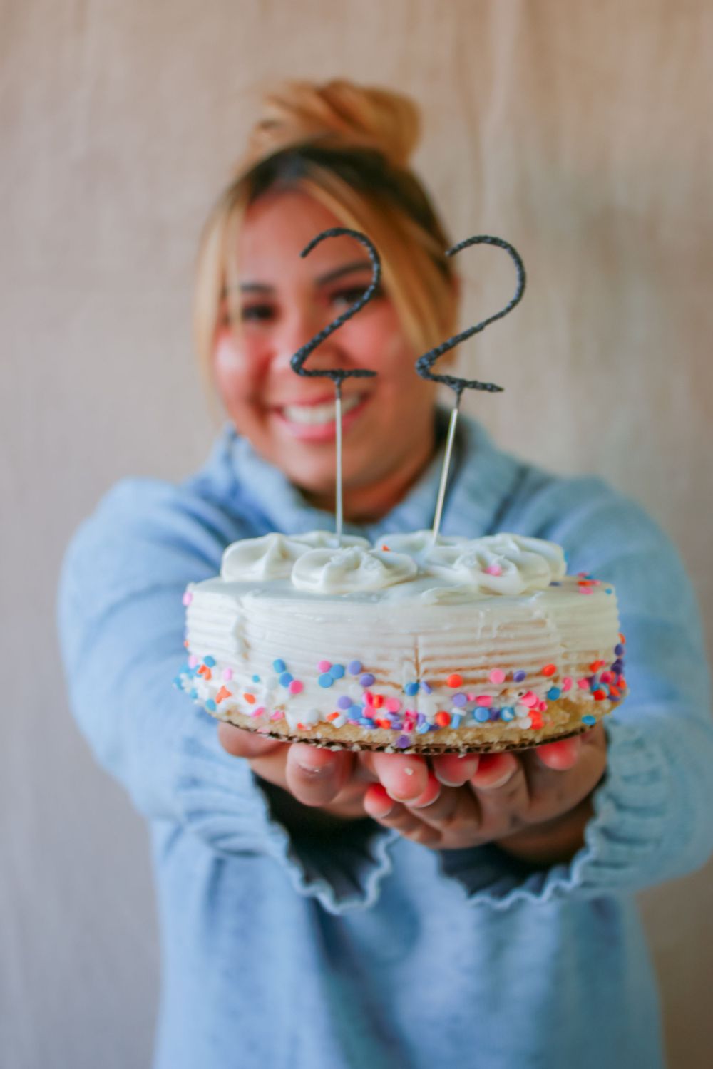 Person holding small white birthday cake with number 22 topper and sprinkle decoration.