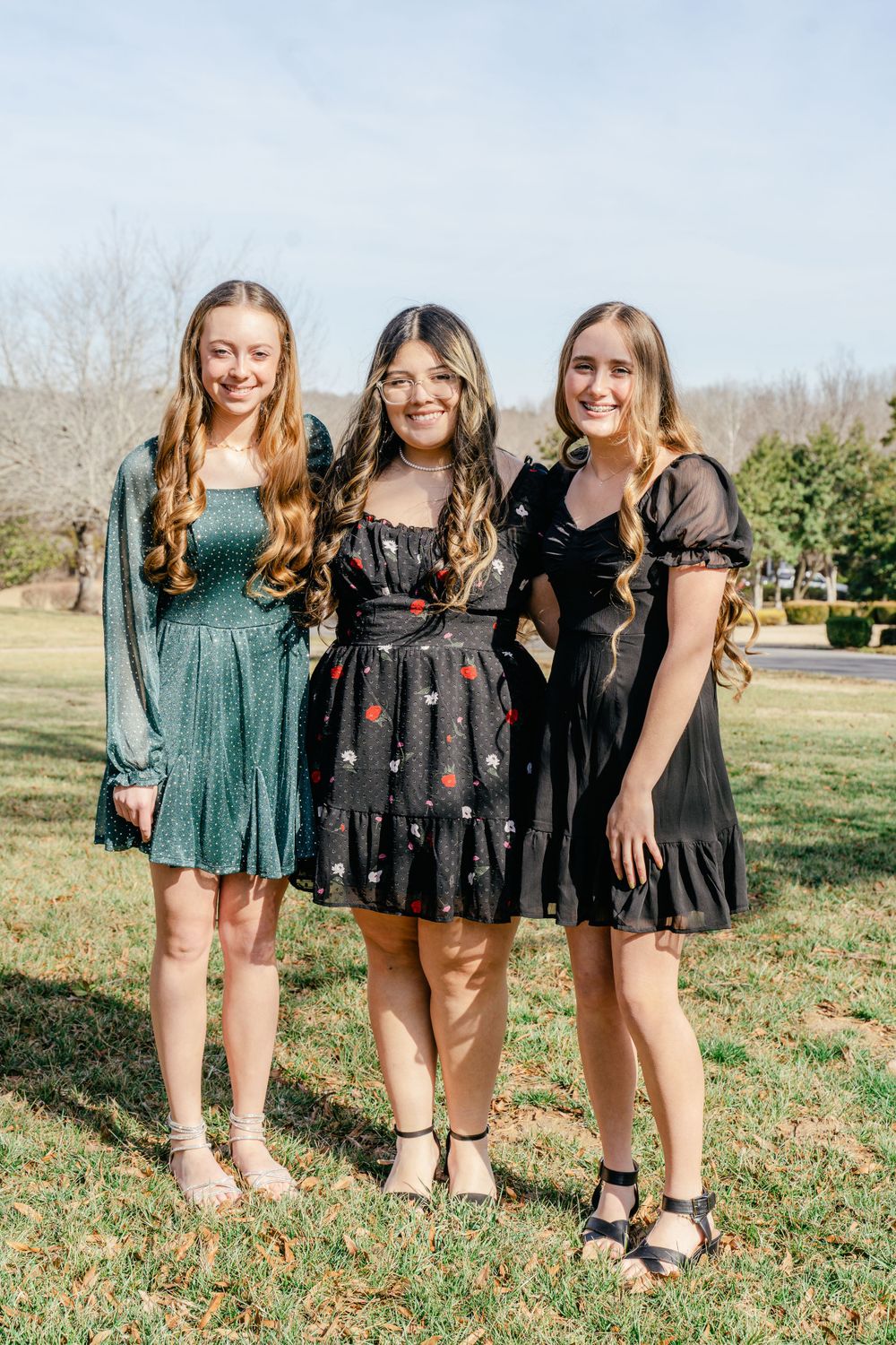 Three friends in stylish dresses posing together outdoors on a sunny day.