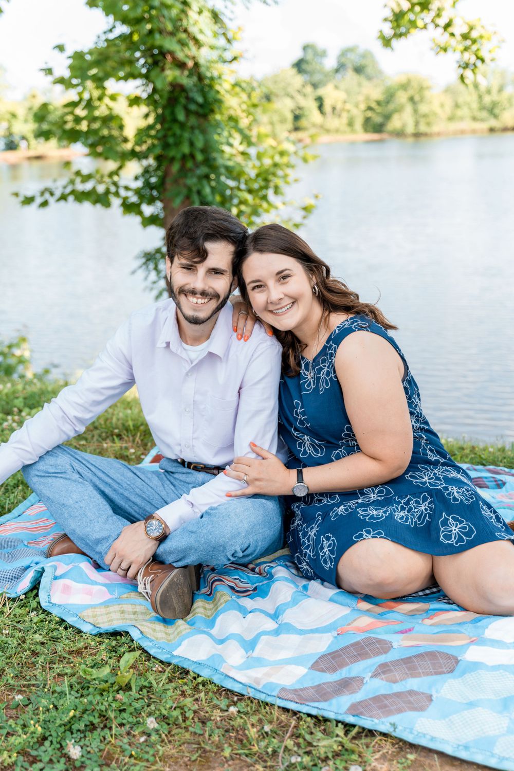 Couple enjoying a romantic picnic by the lake on a patterned blanket.