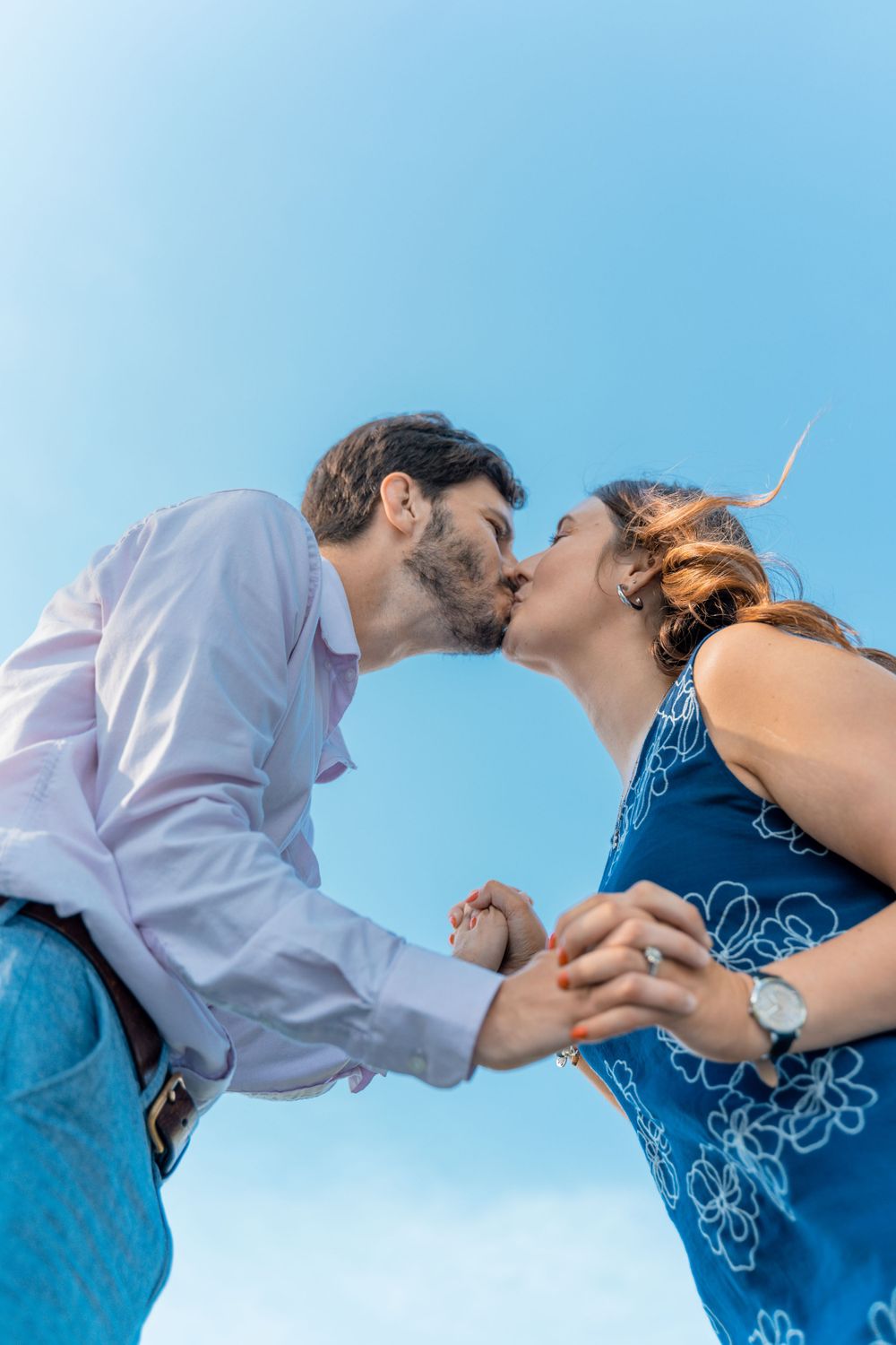 Romantic couple sharing a kiss against bright blue sky background.