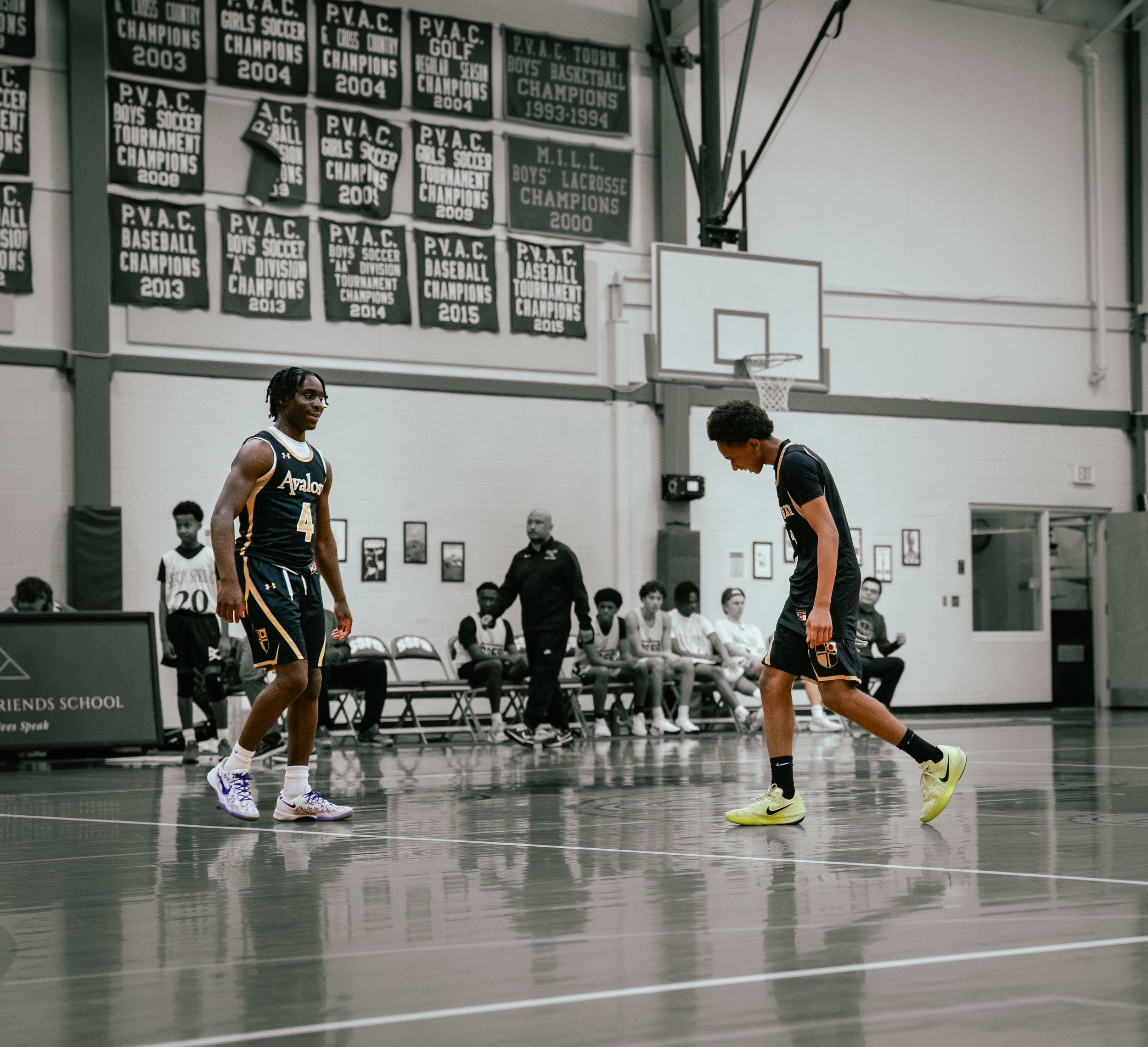 Two basketball players facing off on indoor court with team benches in background.