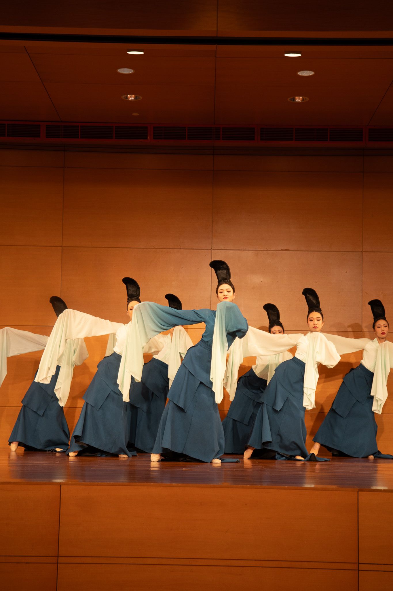 Performers in blue skirts and white flowing sleeves execute a graceful traditional Chinese dance on stage.