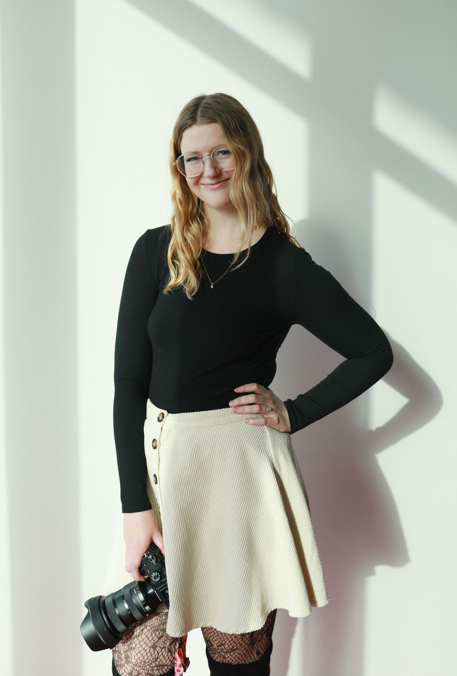 Model wearing black long sleeve top with cream colored dress and floral tights posing in bright studio setting.