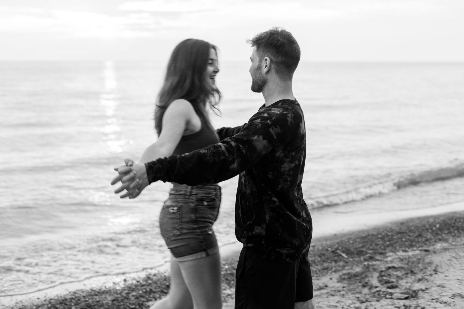 Romantic black and white photo of couple embracing on beach at sunset.