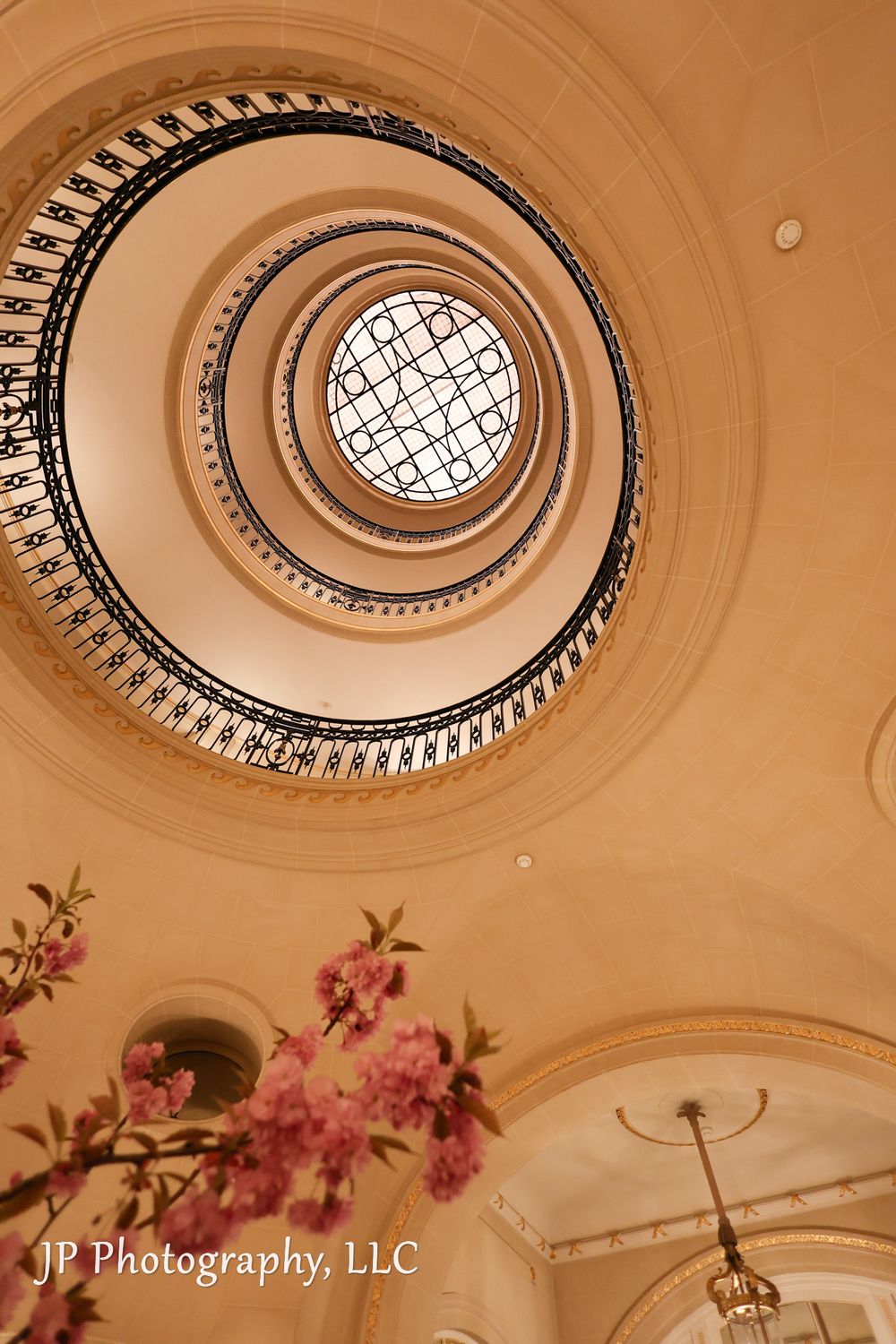 Spiral staircase viewed from below with ornate ceiling details and pink floral accents.