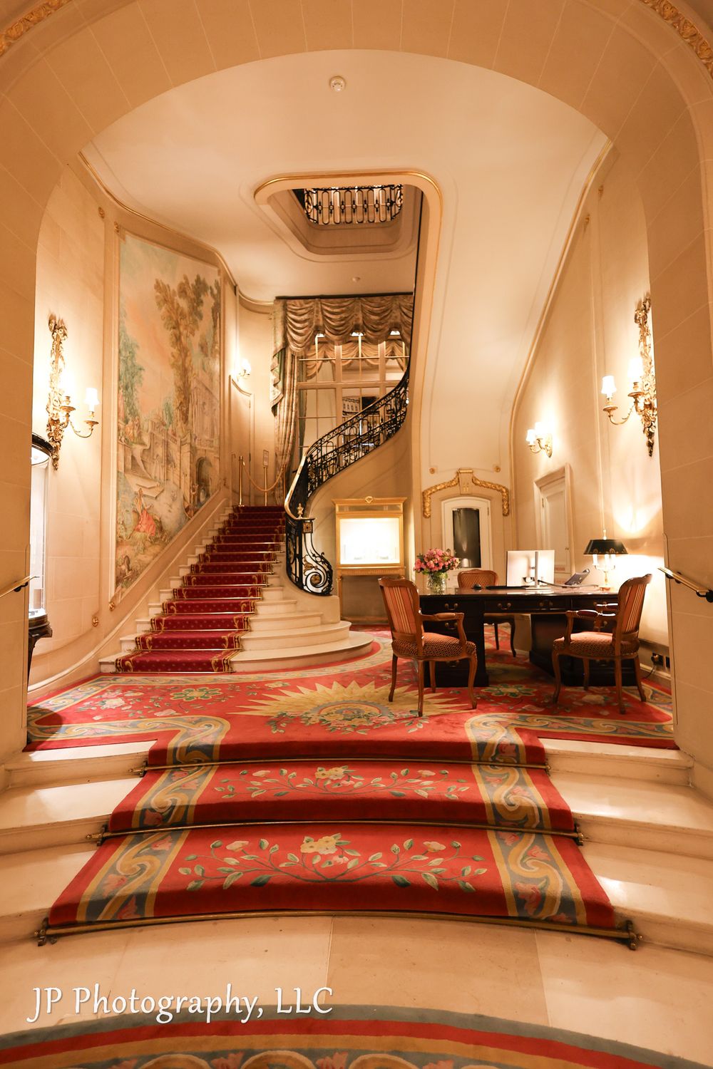 Elegant hotel lobby with grand staircase, red carpeting, and ornate wall decorations.