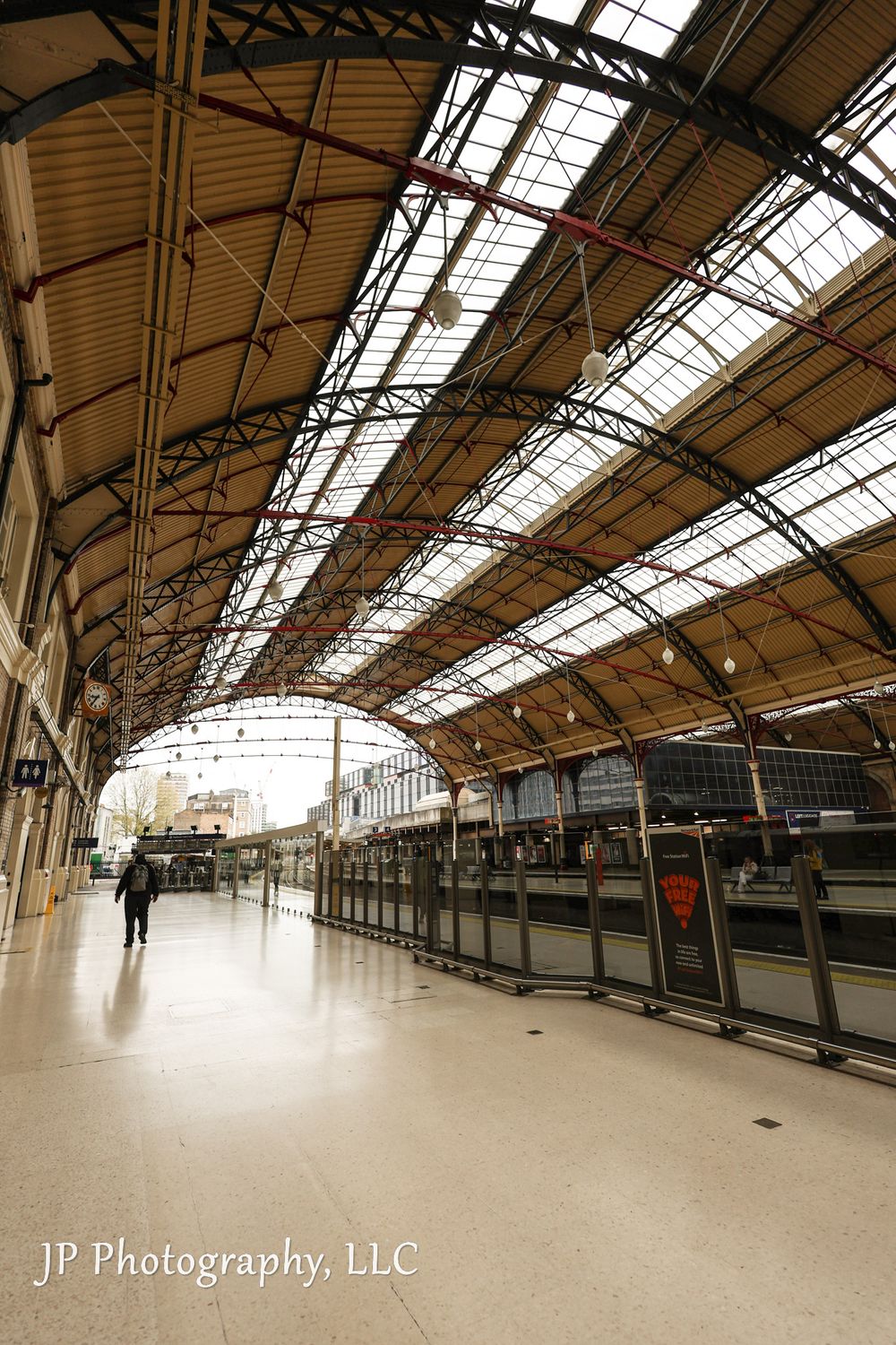 Large empty train station platform with curved glass roof and industrial architecture.