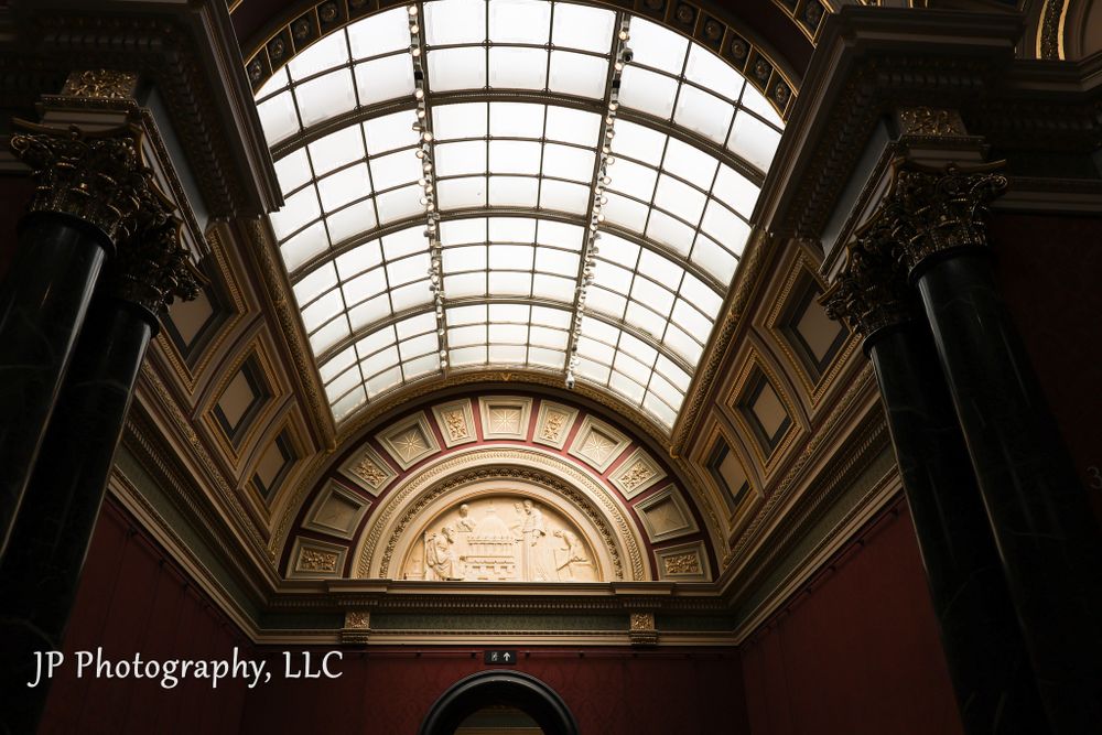 Ornate domed glass ceiling with architectural details in historic building interior.