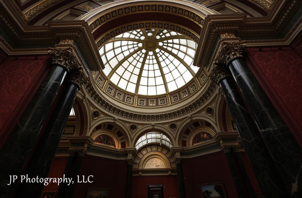 Ornate interior skylight and architectural details of a historic museum gallery with vaulted ceilings.