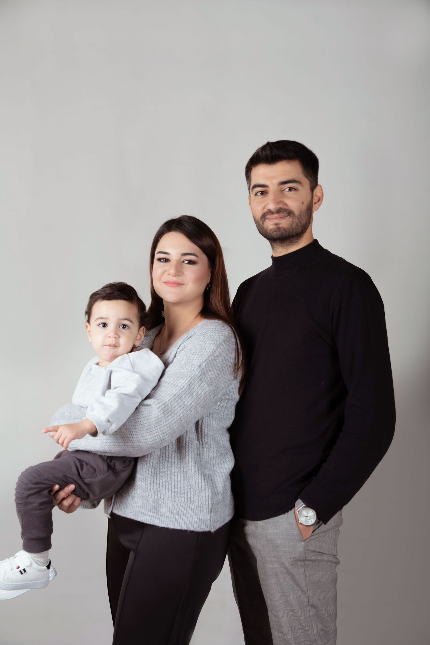 A family portrait against a grey backdrop wearing coordinated casual sweaters.