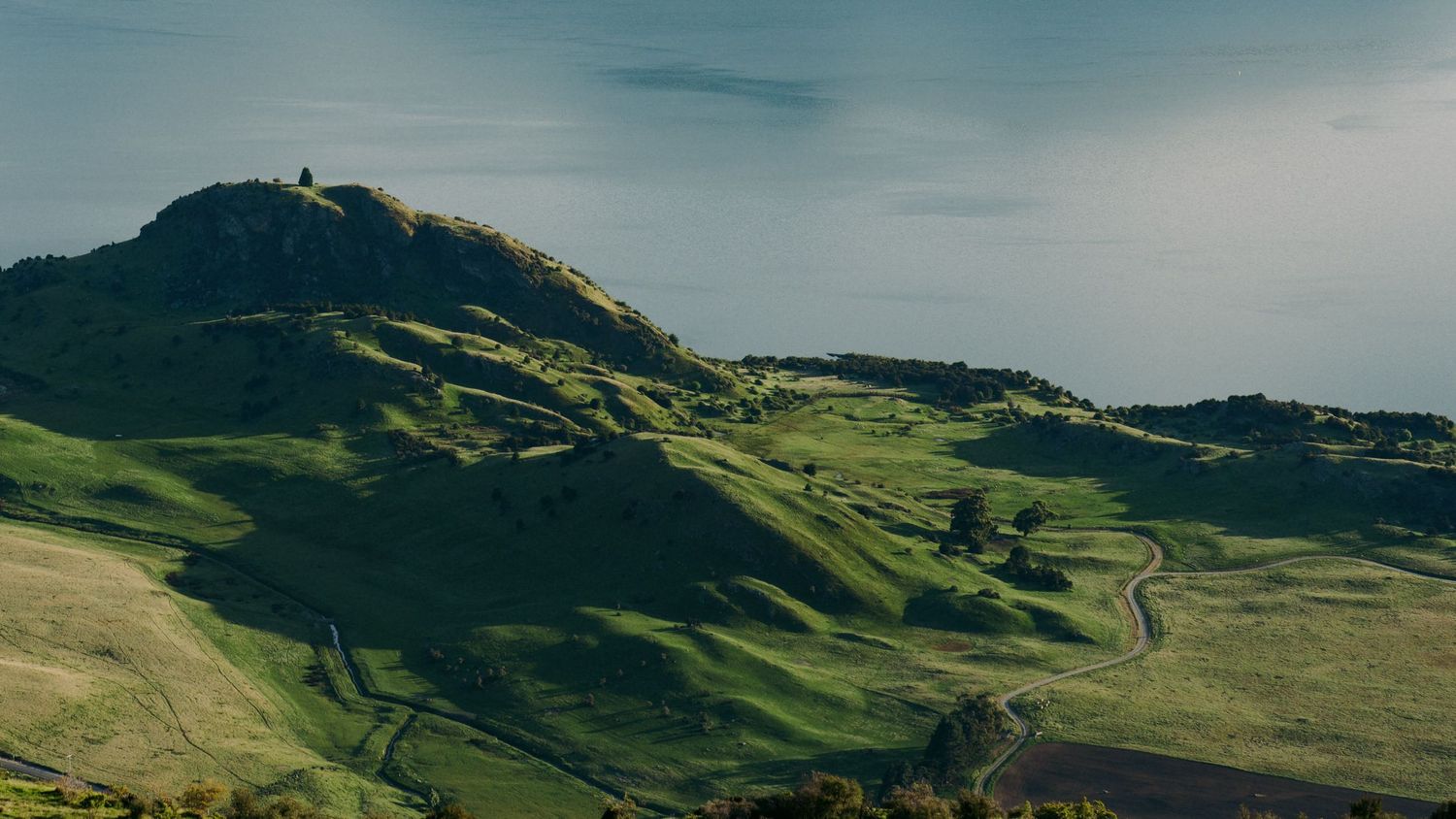Rolling green hills with a lighthouse perched atop the summit against a blue sky.