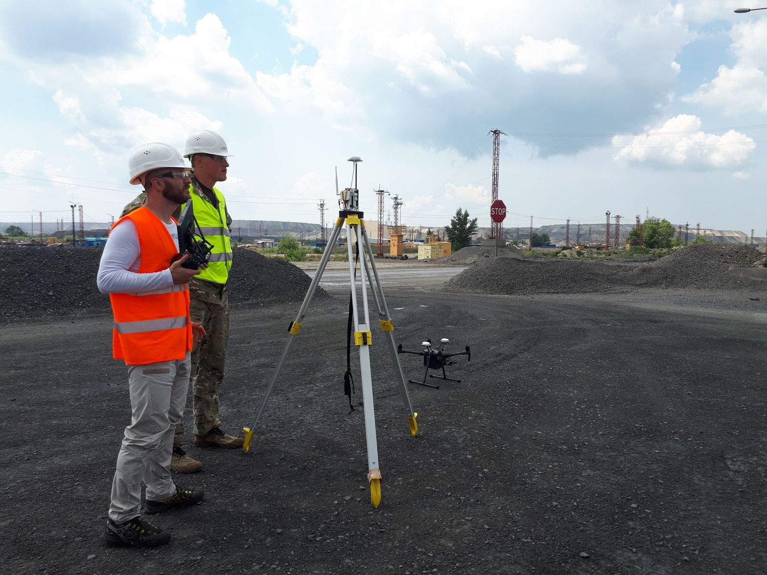 Surveyors using tripod equipment and drone for land measurements on industrial site.