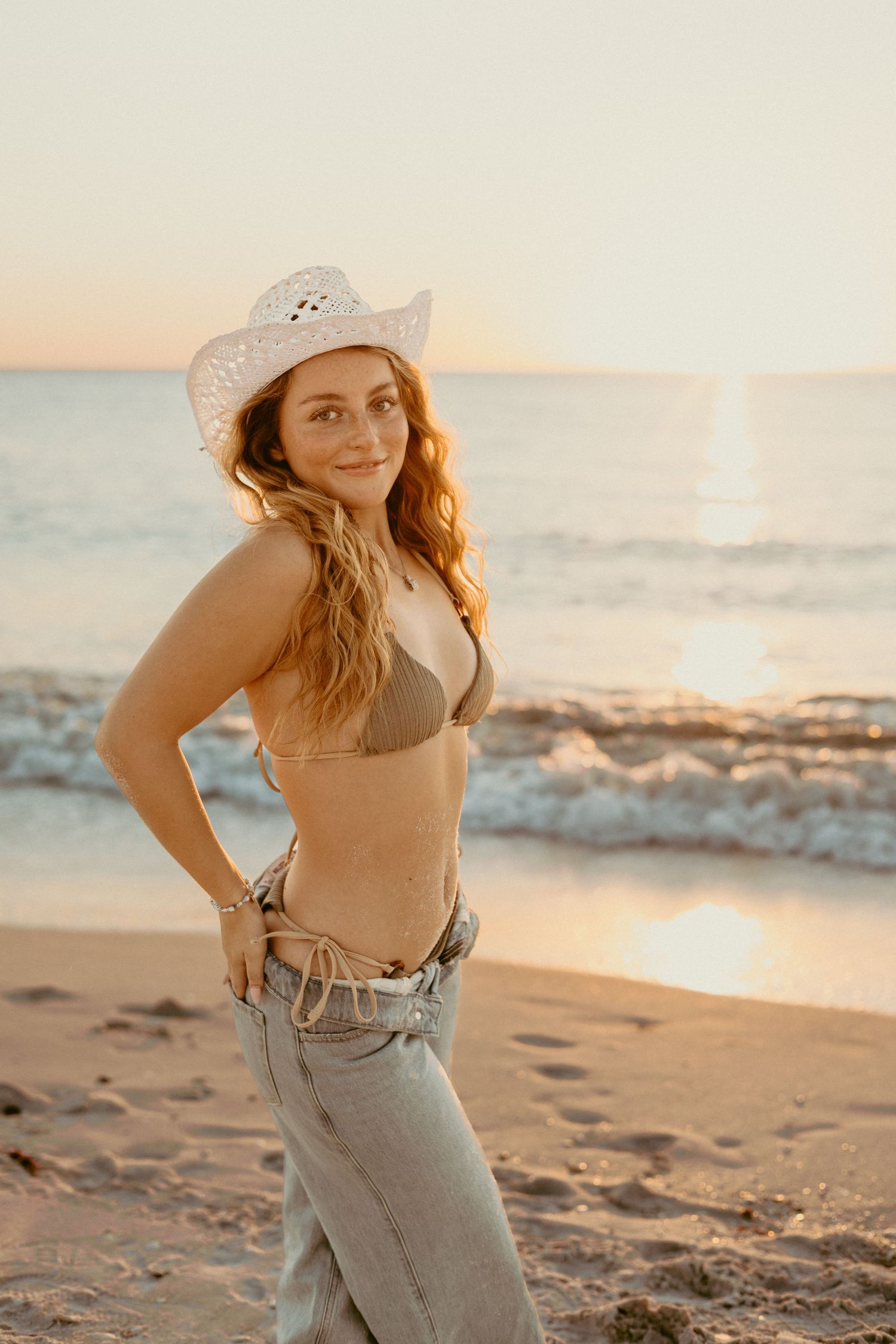 a dirty blonde curly hair girl with white cowgirl hat in front of golden beach