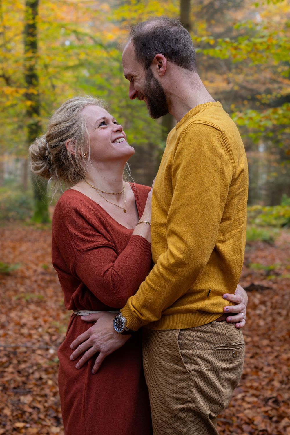A couple in autumn-colored sweaters shares an intimate moment in a forest of fall leaves.
