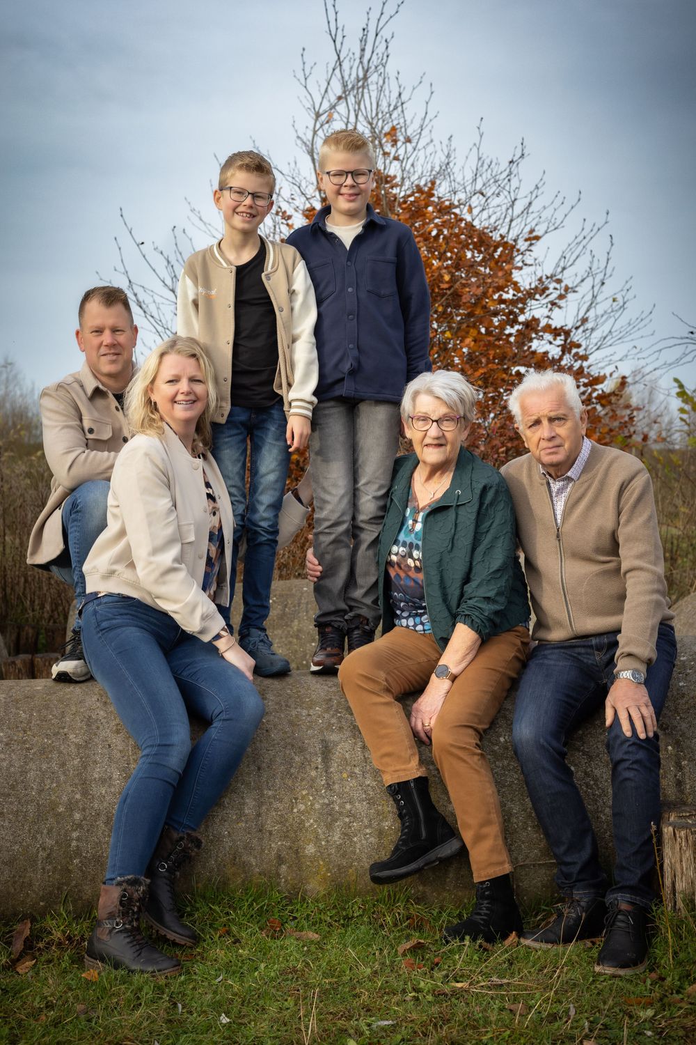 Family group poses together on concrete structure in autumn setting.